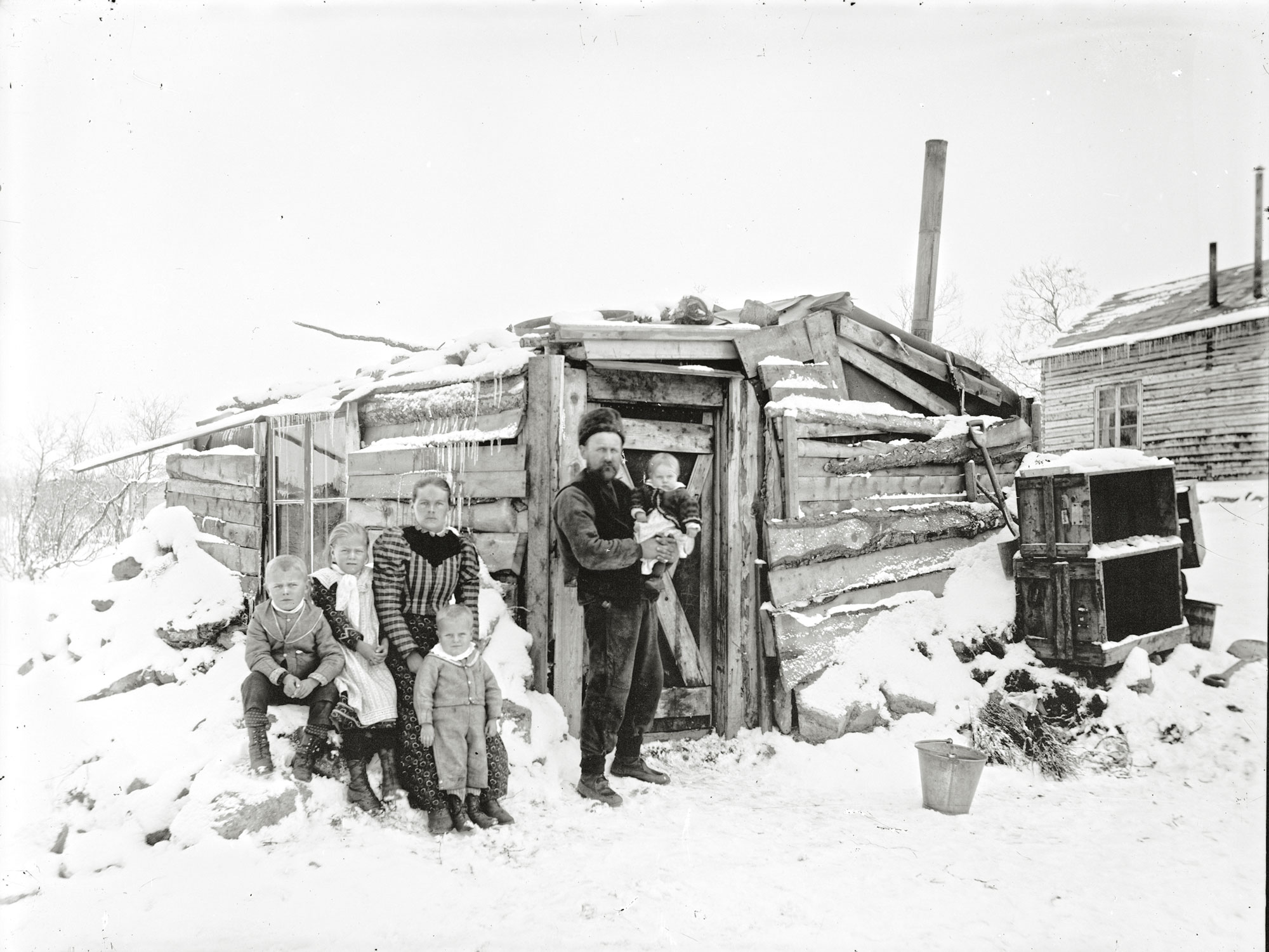 Gruvarbetaren Anders Petter Söderberg och hans fru Ingeborg med fyra barn framför det hem Anders Petter byggt av fläsk- och krutlådor. Dottern Kiruna sitter i pappas famn. Foto: Borg Mesch/Kiruna Bildsamling